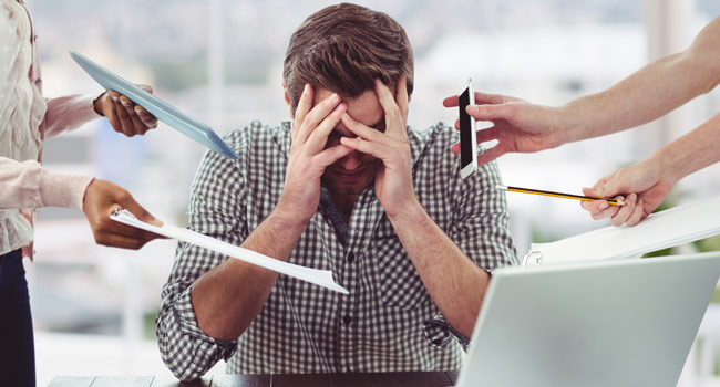 A man sitting on a desk with hands on the forehand, worried and in tension Image